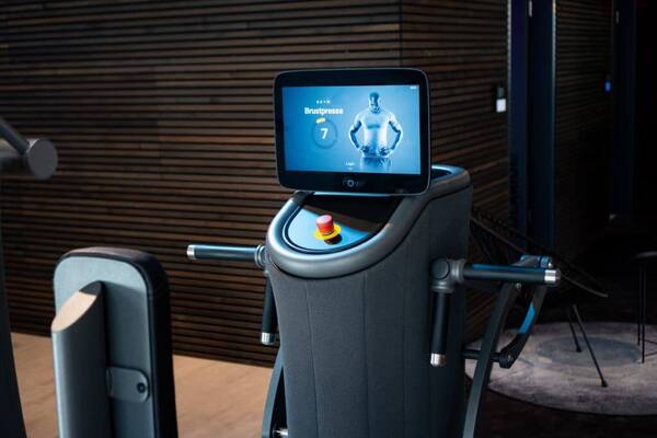 Fitnessgerät im Studio mit Touchscreen „Brustpresse“ und Not-Aus-Knopf